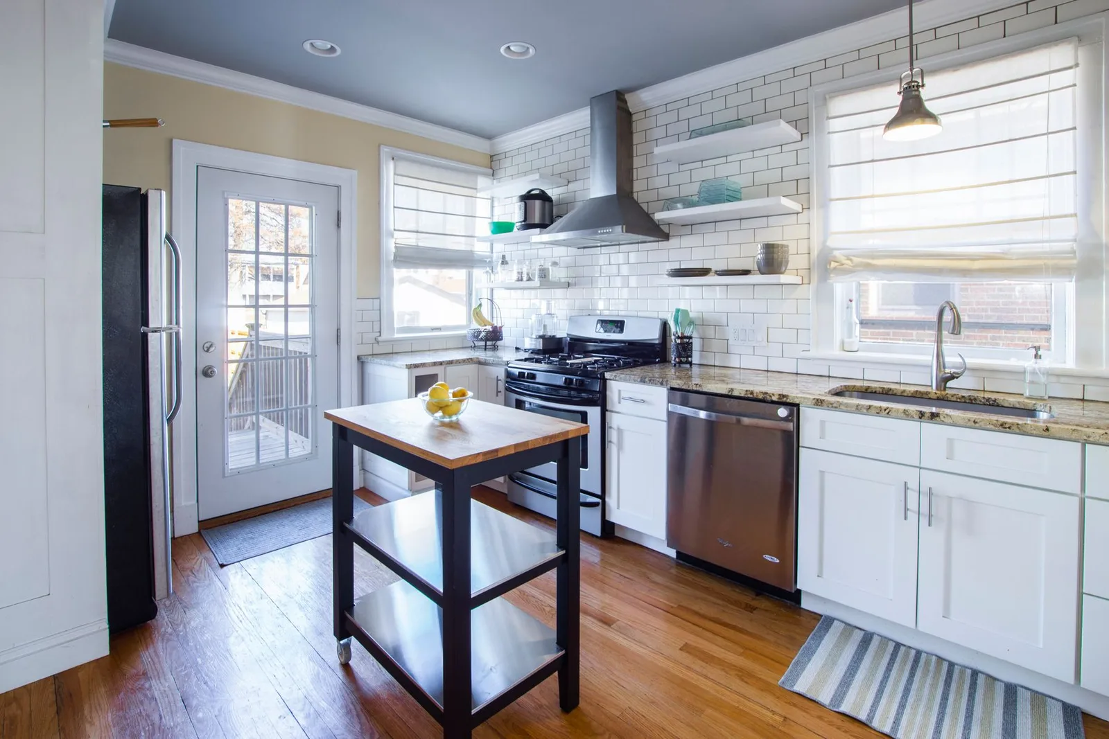 A sunlit home kitchen with white cabinets and a wooden island